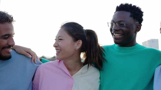Multiracial group of happy young friends having fun together. Millennial generation people from different ethnicities hugging each other while laughing outdoors. Community and friendship lifestyle.