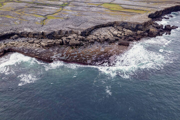 Rough stone coastline with cliffs. Inishmore island, county Galway, Ireland. Popular tourist area with stunning Irish nature scenery. Cloudy sky. Aerial view. Blue ocean surface.