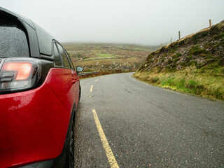 Red car parked on a small country road of Slea Head drive, county Kerry, Ireland. Popular travel...