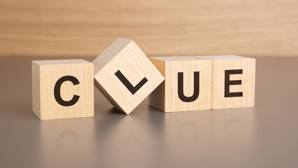 four wooden cubes with the letters CLUE on the bright surface of a brown table, business concept