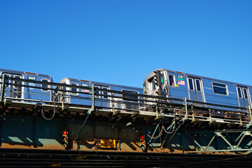 Two shiny bright metal silver elevated subway trains crossing under a clear blue sunny sky. - obrazy, fototapety, plakaty