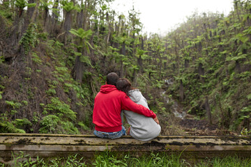 A couple of young people in love are sitting looking at the volcano after the eruption. A new jungle with palm trees is growing on the mountain.