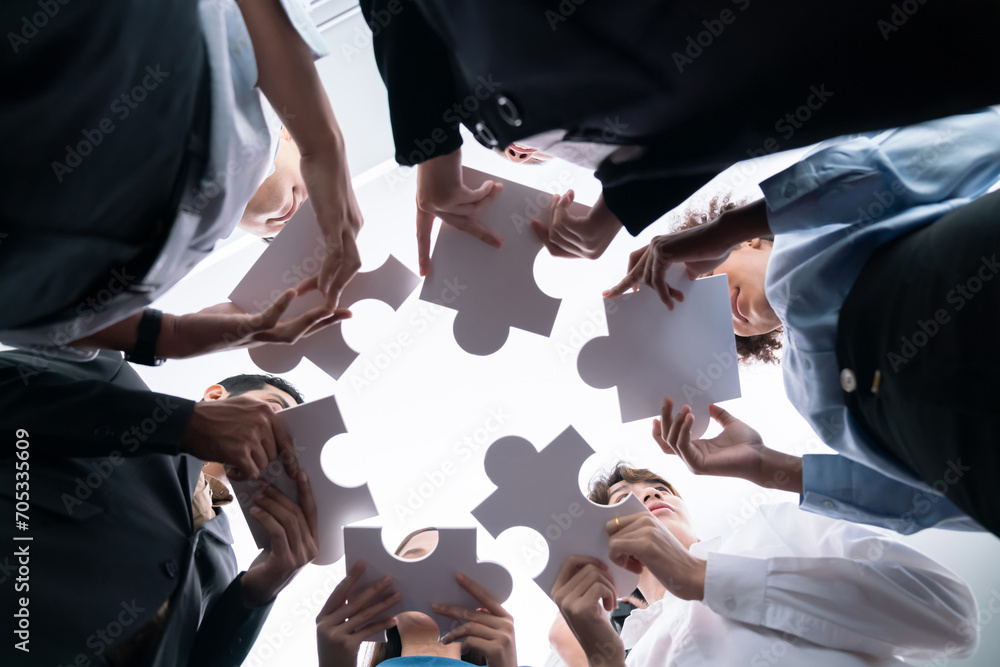 Poster below view of diverse corporate officer workers collaborate in office connecting puzzle pieces as pa
