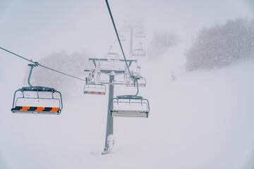 Fototapeta na wymiar Quadruple chairlift rises above snowy forest to misty mountain