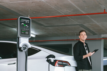Young man travel with EV electric car to shopping center parking lot charging in downtown city...