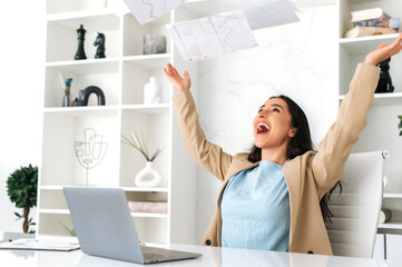 Fototapeta na wymiar Excited happy indian or arabian business woman in elegant clothes, sitting in modern office, rejoicing promotion at work, big profit, cheerfully throws documents, rejoices at success, laughs