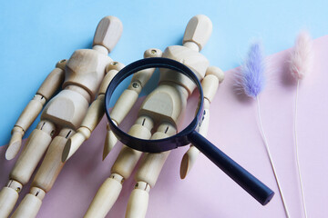 Wooden mannequins and a magnifying glass on a pink and blue background. The concept of gender...