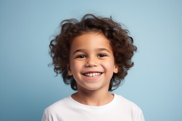 Portrait of cheerful little boy with curly hair on blue background.