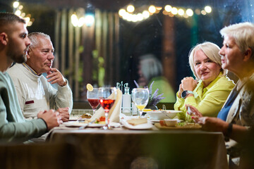 A group of family friends, comprising a young grandson and older individuals, share a delightful dinner in a modern restaurant, exemplifying the concept of healthy aging through intergenerational