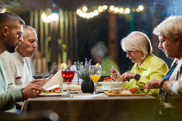 A group of family friends, comprising a young grandson and older individuals, share a delightful dinner in a modern restaurant, exemplifying the concept of healthy aging through intergenerational