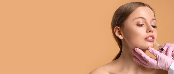 Young woman receiving filler injection in lips against beige background with space for text