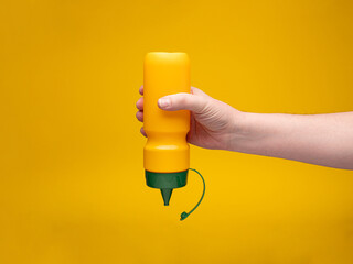 A yellow plastic mustard bottle is hand-held, upside down against yellow background. The lid is...
