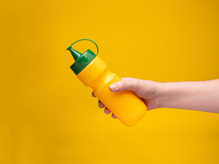 Yellow plastic bottle. Hand holds the bottle. No face.
