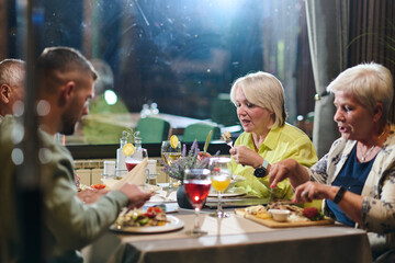 A group of family friends, comprising a young grandson and older individuals, share a delightful dinner in a modern restaurant, exemplifying the concept of healthy aging through intergenerational