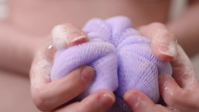 Purple loofah with soap in woman's hands, closeup