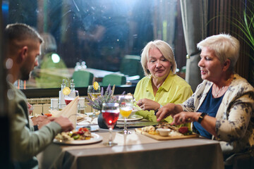 A group of family friends, comprising a young grandson and older individuals, share a delightful dinner in a modern restaurant, exemplifying the concept of healthy aging through intergenerational