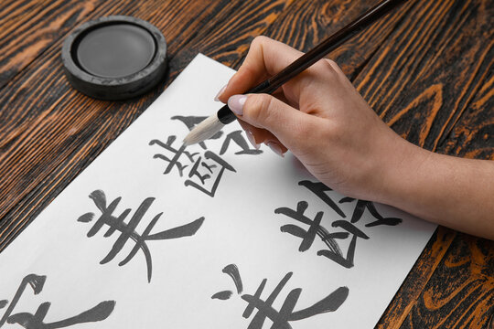 Female hand with Asian hieroglyphs, brush and ink on wooden background, closeup. International Haiku Poetry Day
