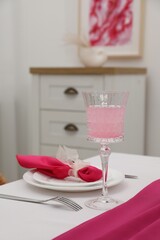Table setting. Glass of tasty beverage, plates with pink napkin and cutlery in dining room