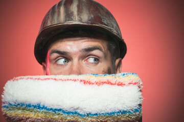 Professional painting. Closeup portrait of surprised male painter in hard hat with paint roller....