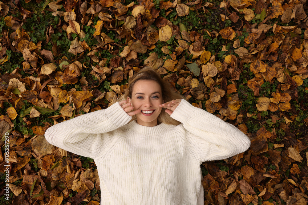 Wall mural Smiling woman lying among autumn leaves outdoors, top view