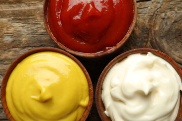 Bowls of ketchup, mayonnaise and mustard on wooden table, closeup