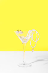 Glass with pearl jewelry on table against yellow background