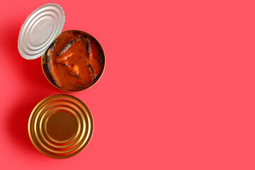 Tin cans with fish in tomato sauce on red background