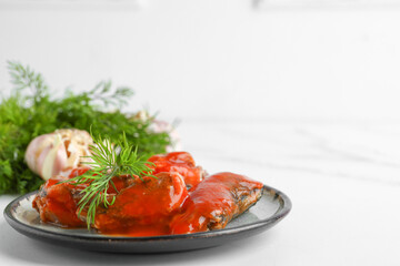 Plate with canned fish in tomato sauce and dill on white table