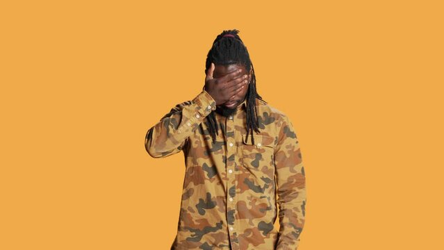 African american guy shows three wise monkeys sign standing over orange background, presenting symbol to not see, hear or speak. Serious person covering his mouth, eyes and ears on camera.