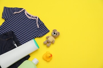 Bottles of laundry detergents, baby clothes and toy bear on yellow background, flat lay. Space for...