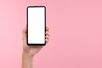 Woman holding smartphone with blank screen on pale pink background, closeup. Mockup for design