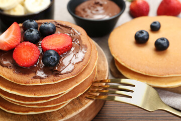 Tasty pancakes with chocolate paste, berries and fork on wooden table, closeup