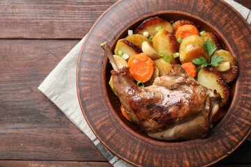Tasty cooked rabbit meat with vegetables on wooden table, top view. Space for text