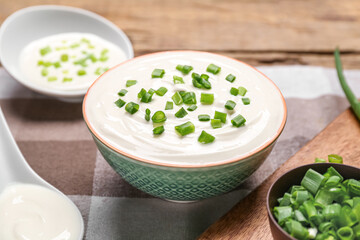 Bowl of tasty sour cream with green onion on table
