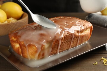 Glazing tasty lemon cake at wooden table, closeup