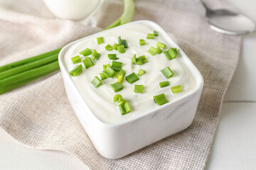 Square bowl with sour cream and sliced green onion on white wooden table