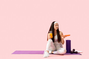 Sporty young woman with glass of vegetable juice and carrot on pink background