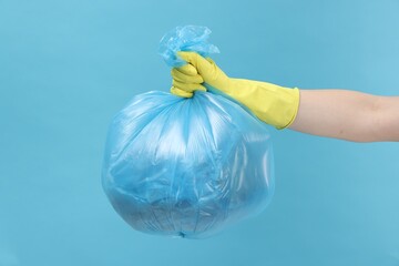 Woman holding plastic bag full of garbage on light blue background, closeup