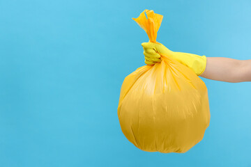 Woman holding plastic bag full of garbage on light blue background, closeup. Space for text