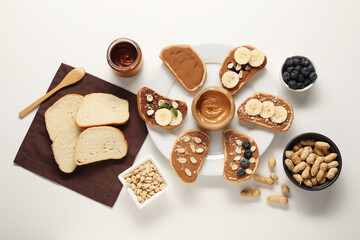 Toasts with different nut butters, banana slices, blueberries and nuts on white table, flat lay