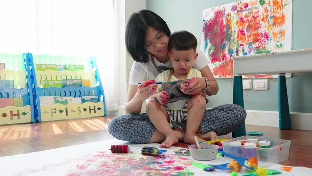 Cheerful Asian Japanese Mother and son Enjoying painting art at home together. Happy Woman coloring on little child boy hand.
