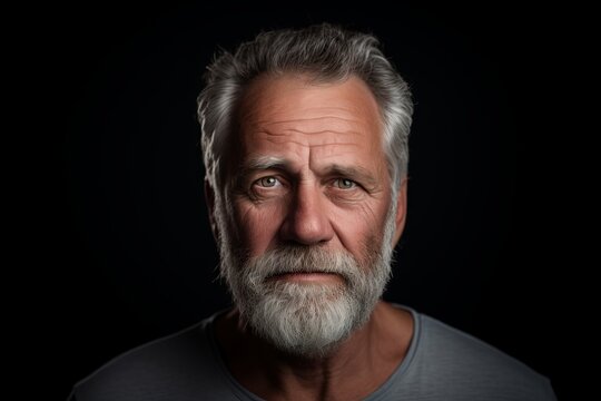 Portrait of a senior man with grey beard on a black background.