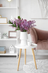 Vase with blooming lilac flowers and cup of tea on coffee table in interior of living room