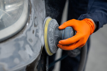 A mechanic sands the putty on a car body with a machine. Repair after an accident. 