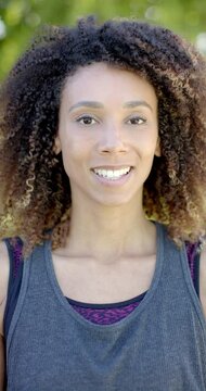 Vertical video portrait of biracial woman with long curly hair smiling in sunny garden, slow motion