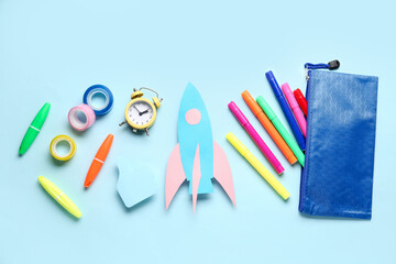 Paper rocket with pencil case and different stationery on blue background