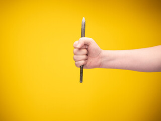 Hand holding a chisel for stone work. No face, yellow background. 
