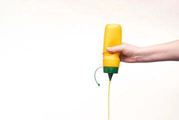 A plastic mustard bottle is hand-held, upside down. The mustard is Squeezed out. Copy space.
