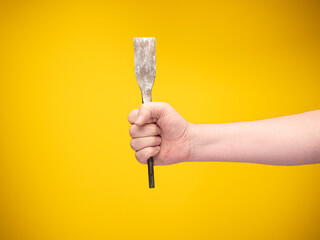 Workman holding a flat chisel for stone work on a construction site. No face, yellow background. 
