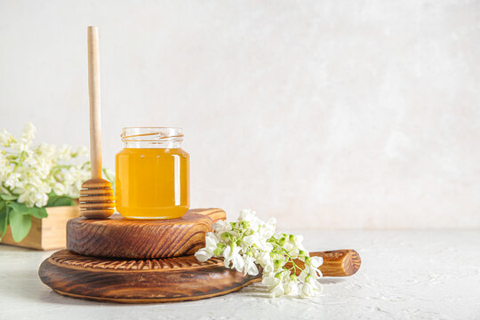Jar of honey with flowers of acacia and dipper on light background